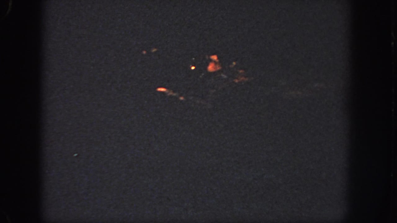 1951 Atlanta 8mm frame showing the swimmer reduced to a dim shape with small orange highlights on the water.