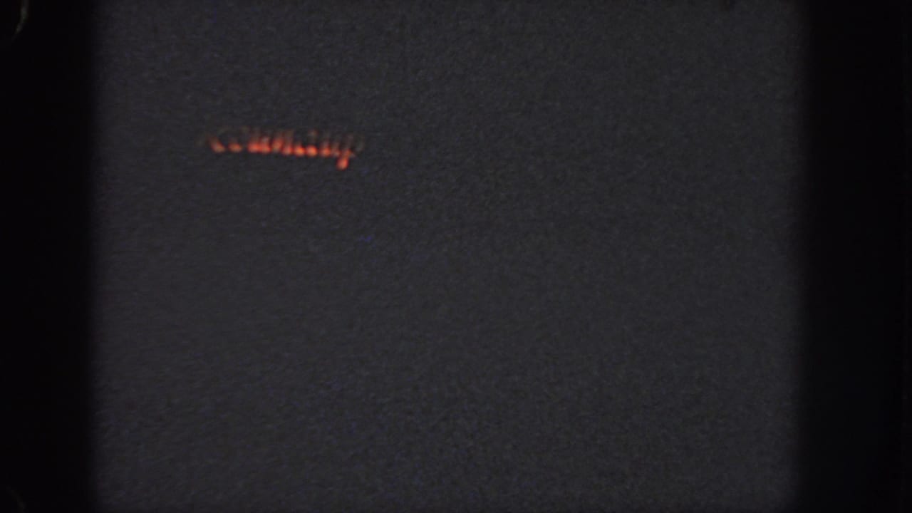 1951 Atlanta 8mm frame with a faint red-orange light streak, possibly part of a holiday display, in darkness.