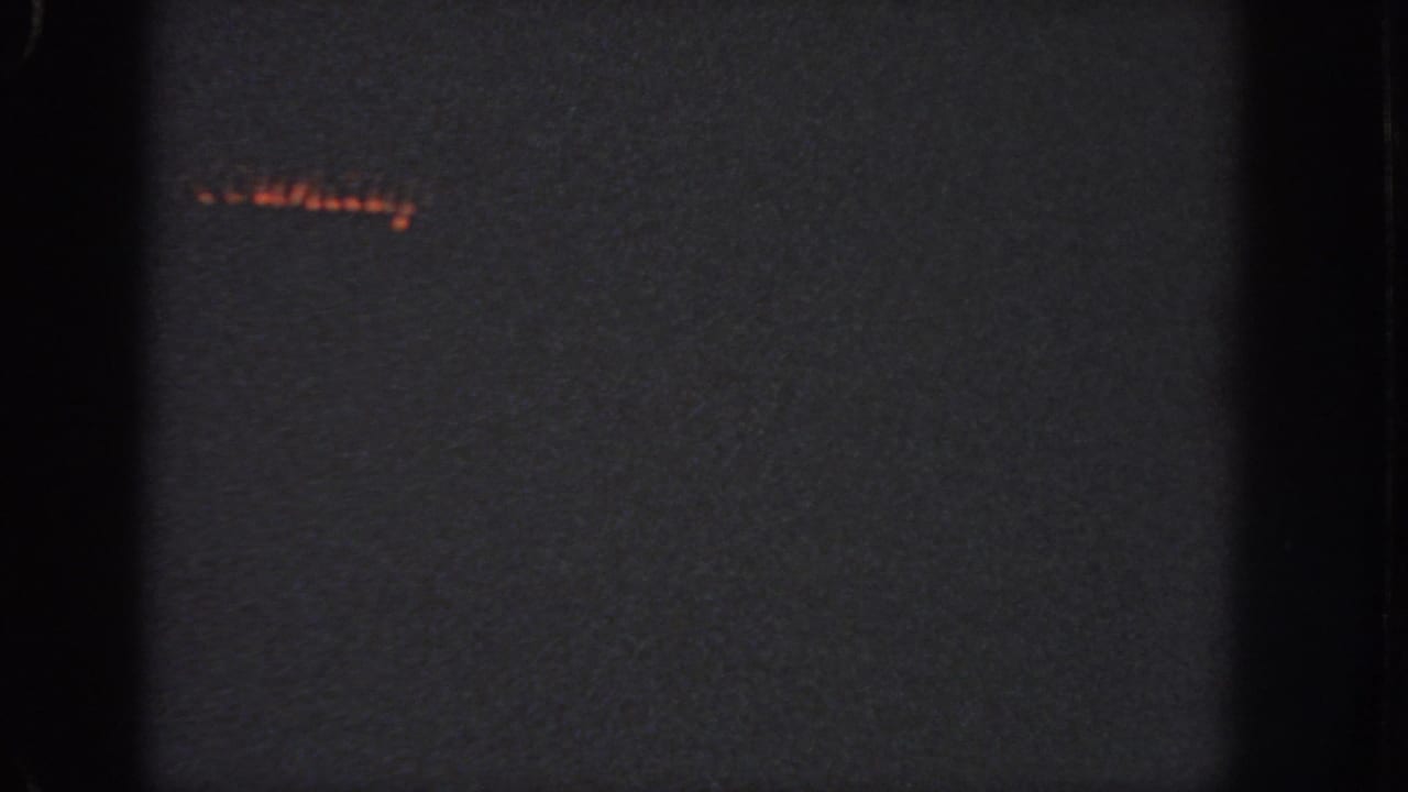 1951 Atlanta 8mm frame showing a mostly dark field, faint red light at upper left, grain, vignetting, and black film-edge bands.
