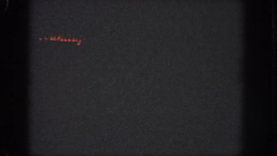 1951 Atlanta 8mm frame showing a mostly dark field, faint red light at upper left, grain, vignetting, and black film-edge bands.