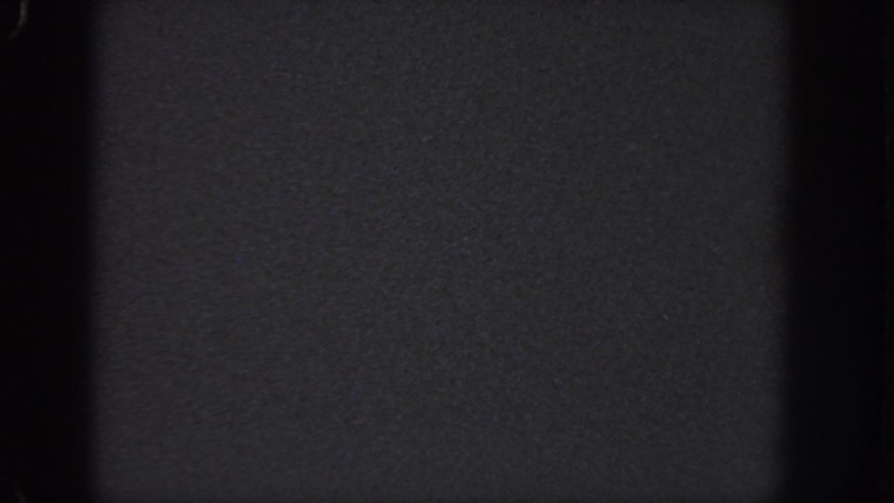 Near-blank 8mm frame from the Atlanta 1951 source, with dark grey texture, dust specks, and black vertical gate edges.