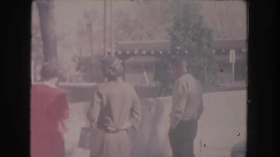 The adults remain grouped outdoors in New Mexico, partly turned away as they watch or discuss something beyond the camera view.