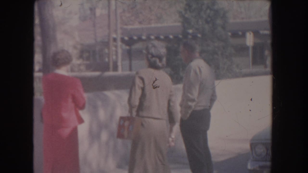 Two women and a man walking away beside a low wall near a building.