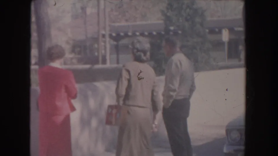 In 1951 New Mexico home-movie footage, two women and a man walk outdoors near a low wall, with one woman in red and another carrying a handbag.