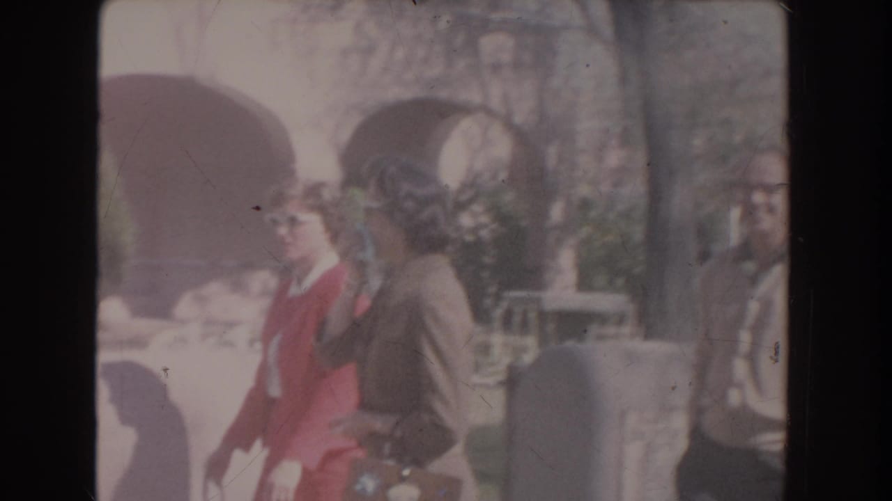 Two women in mid-century clothing appear near arched exterior openings, one wearing a red dress and white sunglasses and the other in a brown suit.