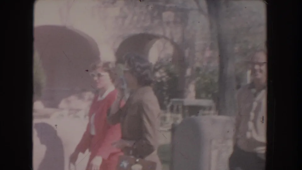 Two women in mid-century clothing appear near arched exterior openings, one wearing a red dress and white sunglasses and the other in a brown suit.