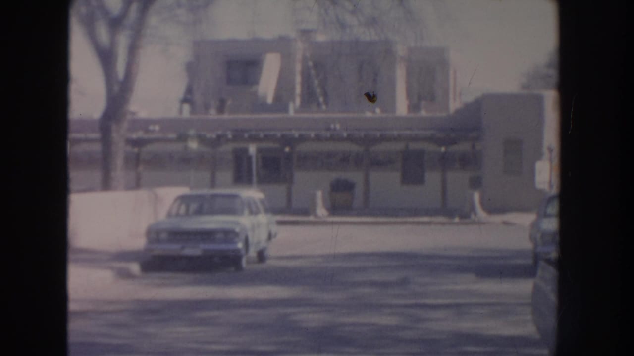 Light-colored car parked in front of a low commercial building with striped awnings.