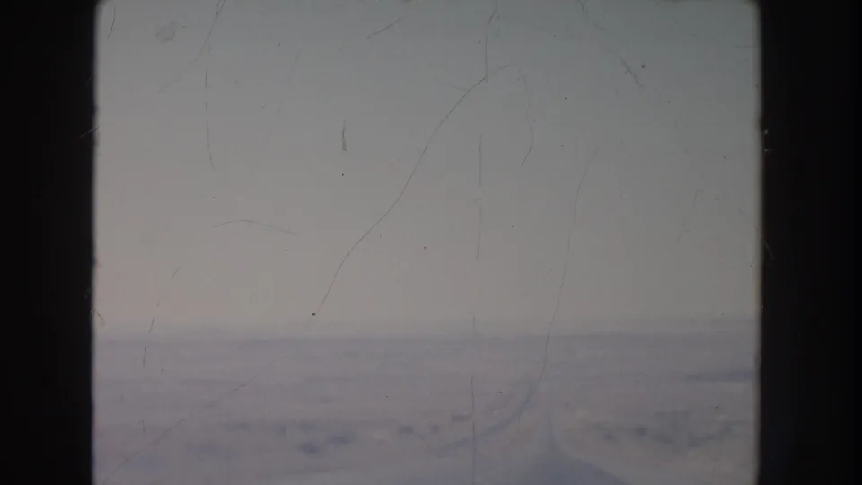 1951 New Mexico desert terrain viewed from inside a vehicle, with window bars framing pale sky and low scrub.