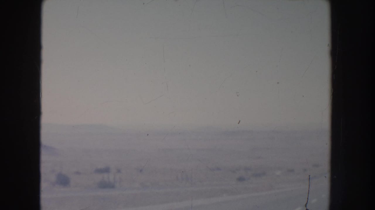 Open desert horizon behind dark window framing with faint road and scattered brush.