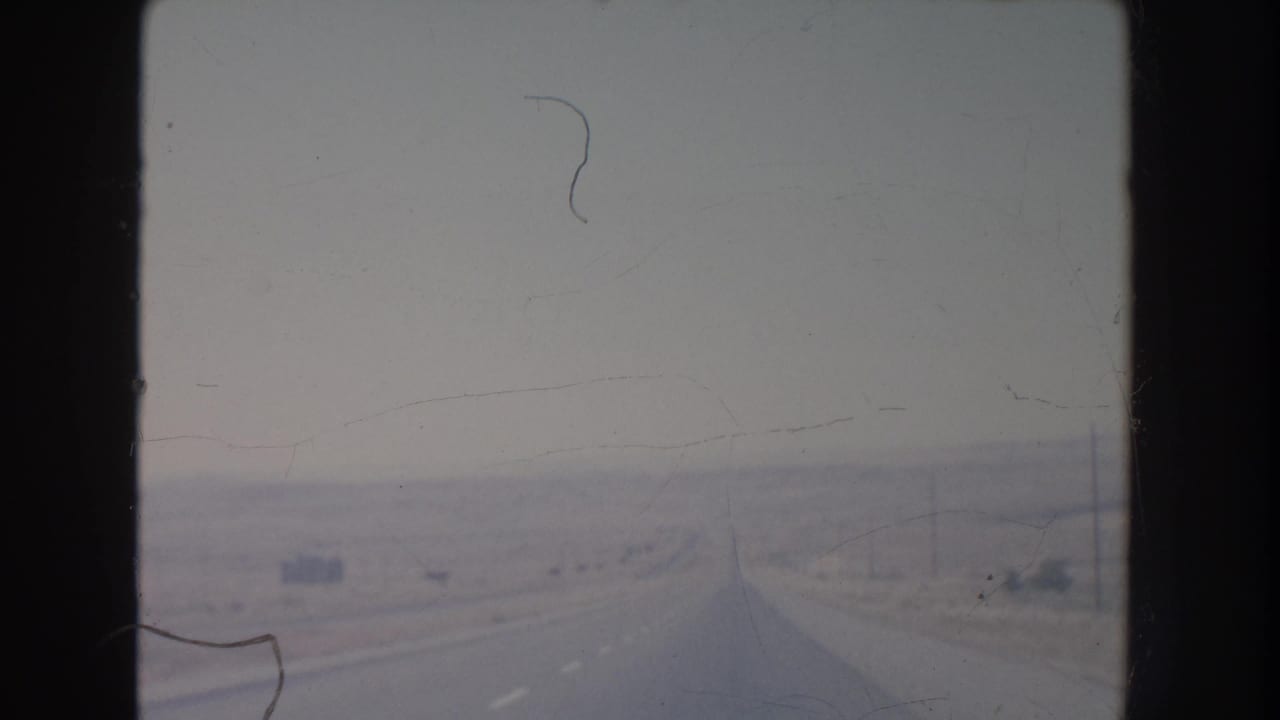Long straight highway receding into a hazy desert landscape with utility poles along the roadside.