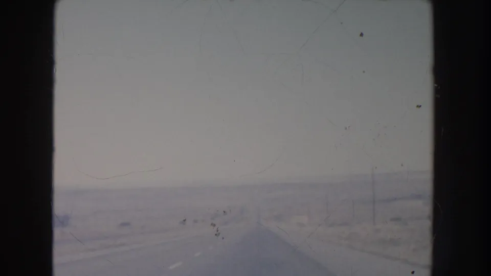 1951 New Mexico driving frame showing an empty paved highway disappearing into a hazy desert horizon with sparse roadside poles.