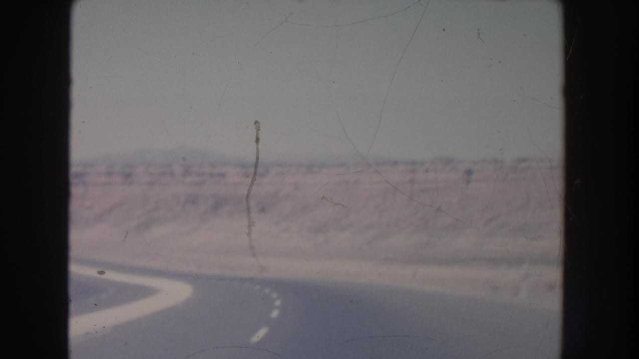 Desert highway curve seen from a moving vehicle with mesas beyond.