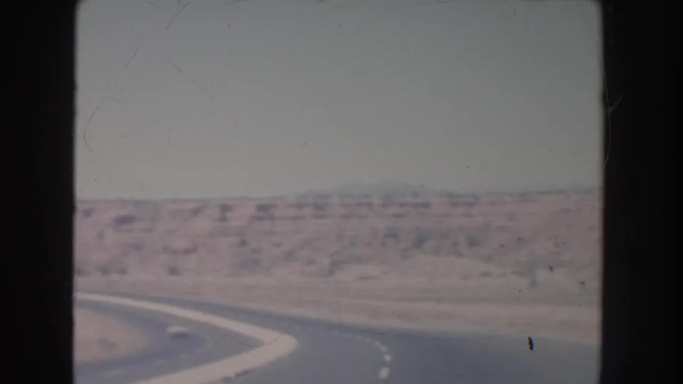 1951 desert travel view showing a sweeping road curve, arid foreground, and low mesas under a washed-out sky.