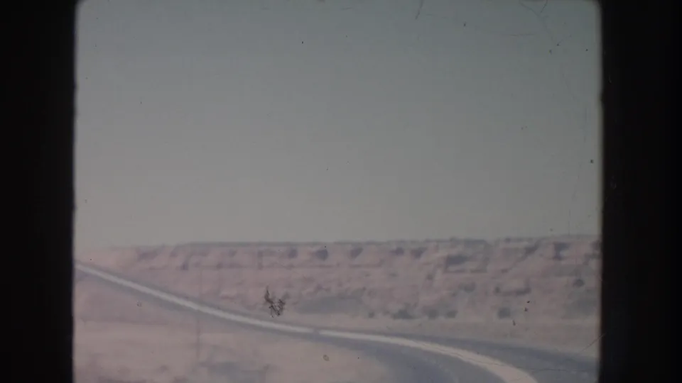 Faded 8mm frame from New Mexico showing a road line receding through desert terrain with mesas across the horizon.