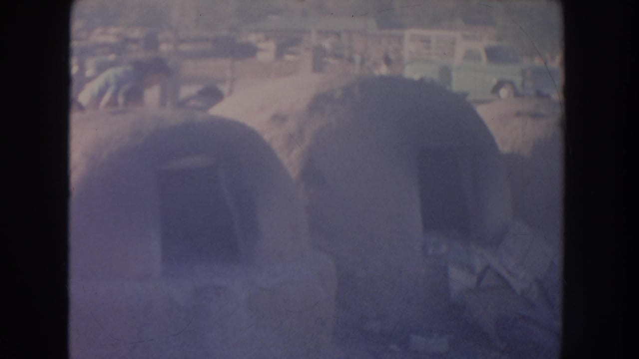 Rounded adobe structures beside a road with parked cars in the background.