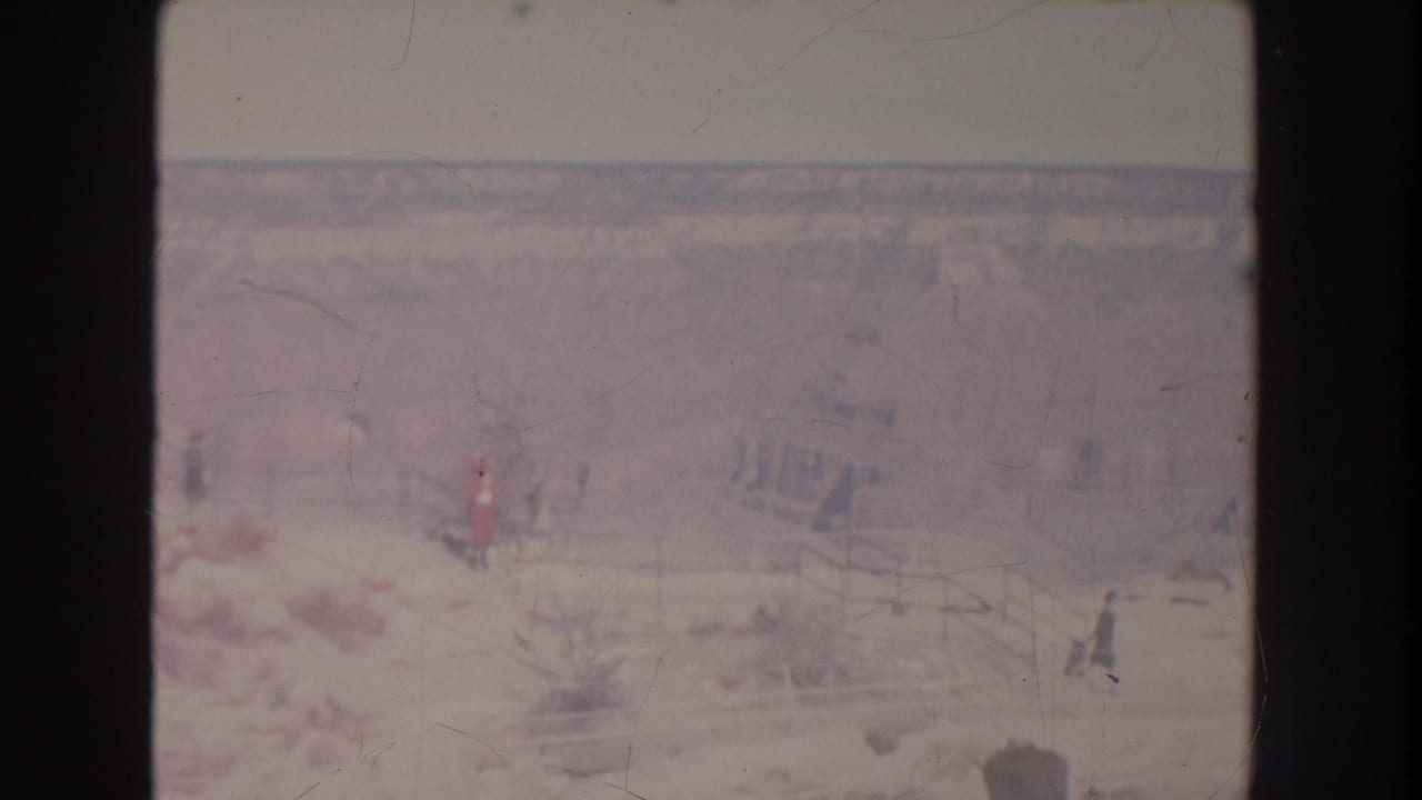 Distant visitors walk along a pale rocky canyon path near a wooden railing.