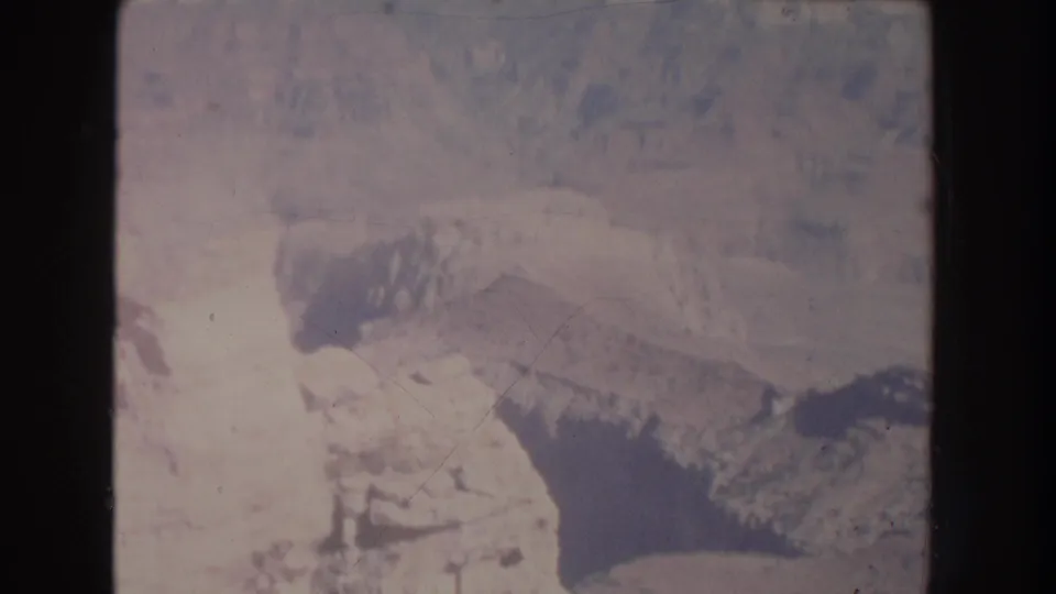 1951 New Mexico home-movie frame showing a hazy canyon ledge, a wooden railing, and a distant visitor near the rocky path.