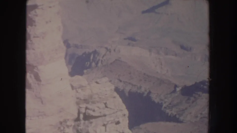 1951 New Mexico 8mm frame showing rugged canyon terrain from above, with sunlit rock faces and deep shadowed formations.
