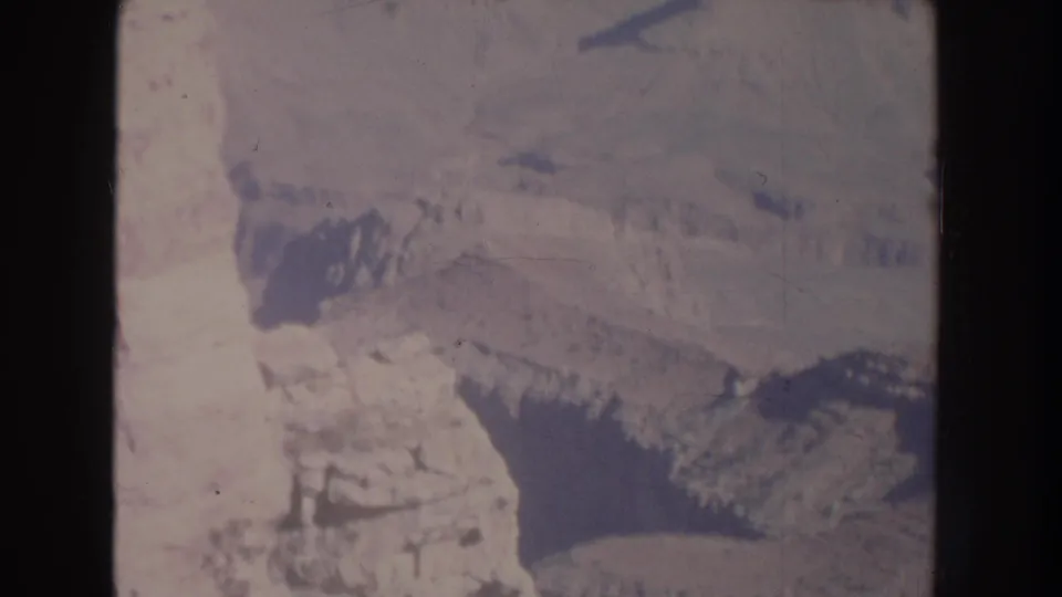 1951 New Mexico aerial home-movie frame with layered rock formations, pale slopes, and broad canyon shadows.
