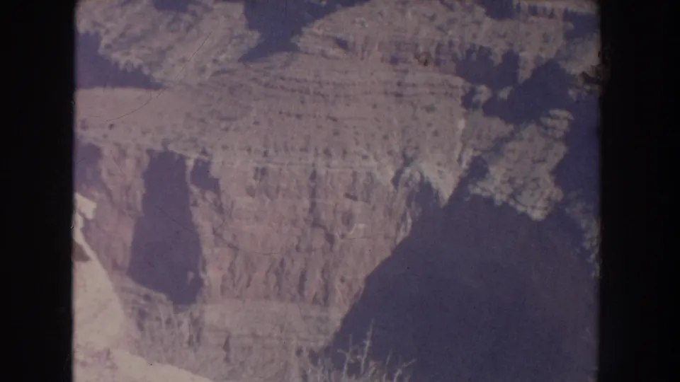 1951 New Mexico 8mm still showing a broad rocky canyon face, steep vertical cuts, and dark shadowed terrain below.