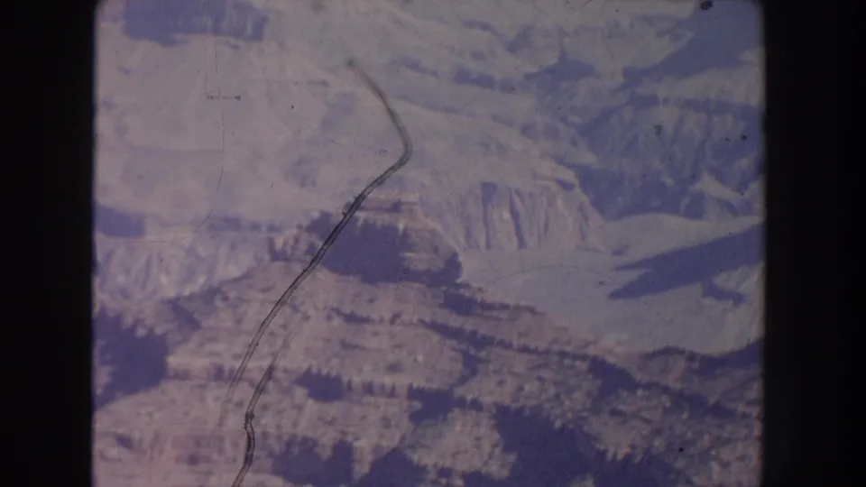 1951 New Mexico aerial frame of rugged canyon slopes and mesas, marked by a curved scratch across the 8mm film surface.