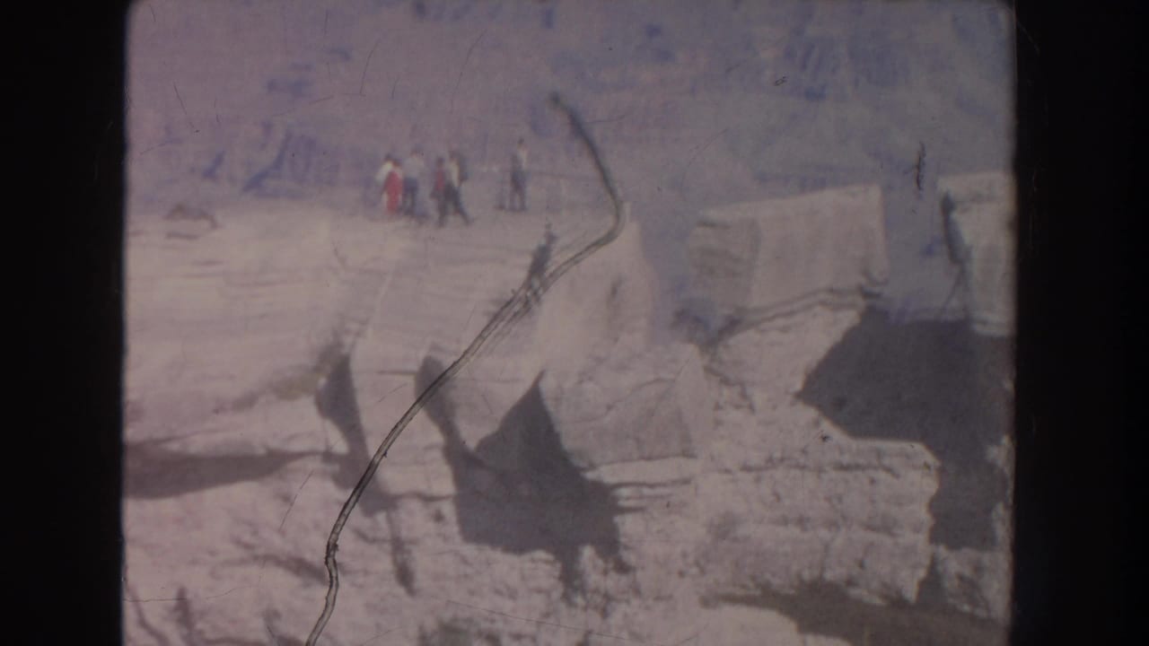 Tourists stand near a pale rocky canyon edge above shadowed stone formations.