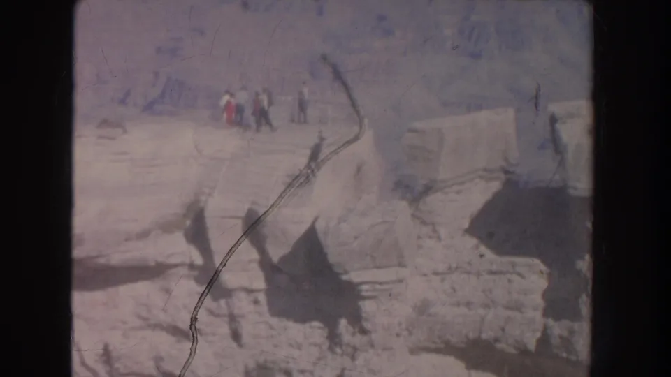 1951 8mm frame of tourists near a rocky canyon overlook in New Mexico, with faded color and visible film scratches.