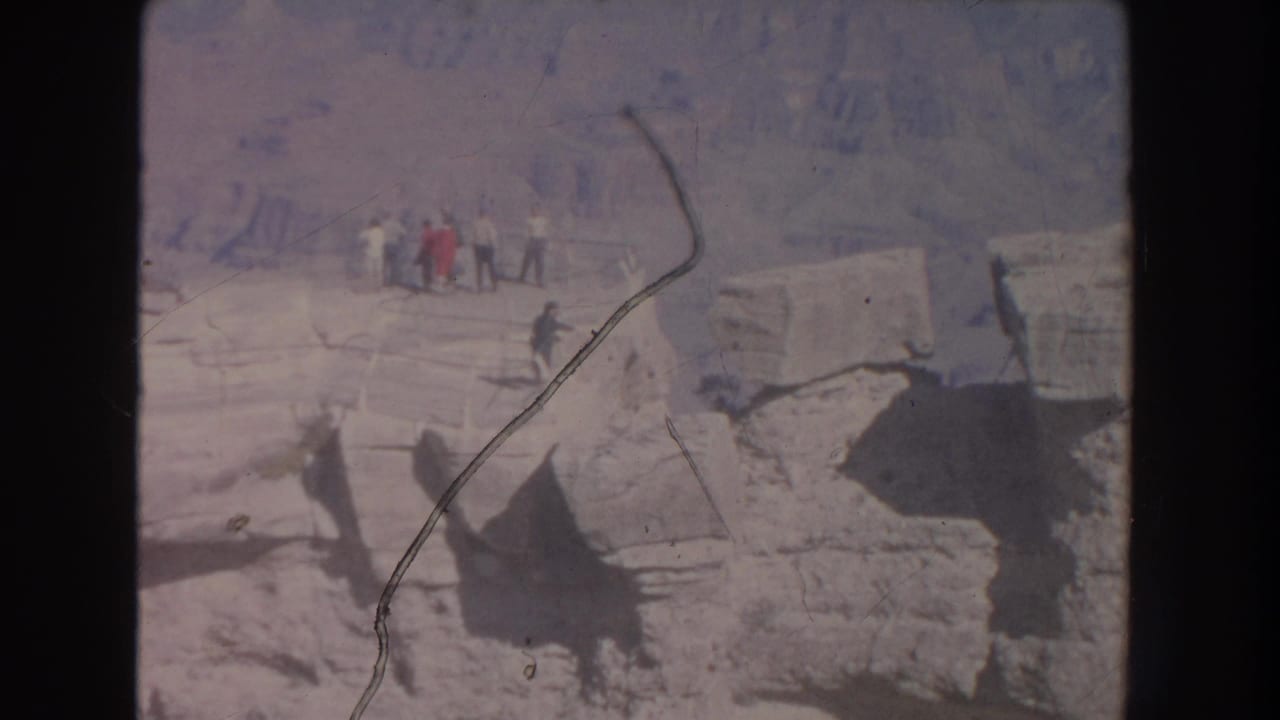 Small group of visitors stands on a canyon rim beside weathered stone ledges.