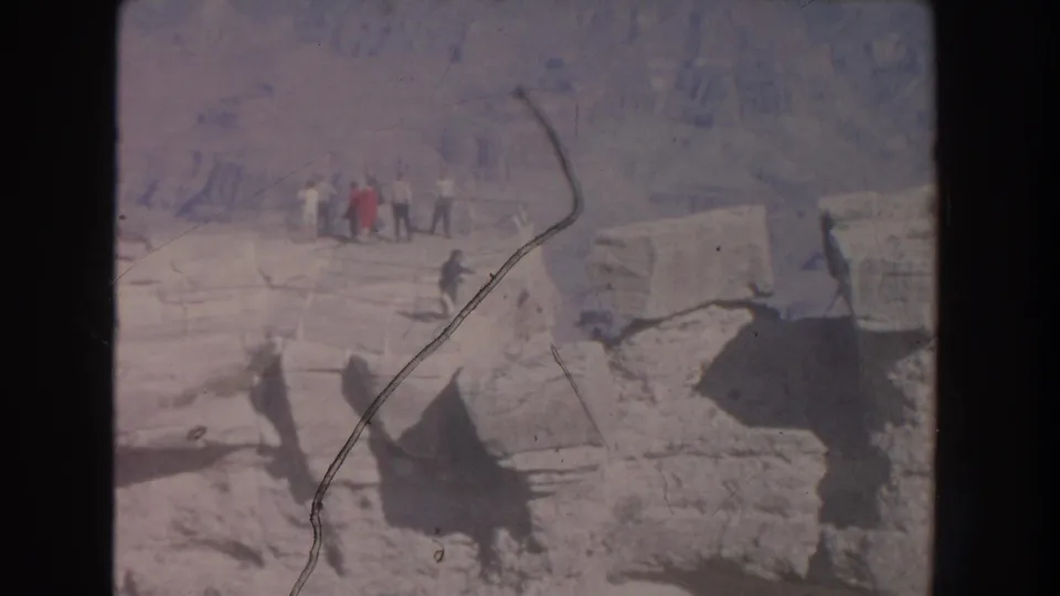 Faded 1951 home-movie frame showing visitors on a New Mexico canyon rim, seen from a distance across pale rock.