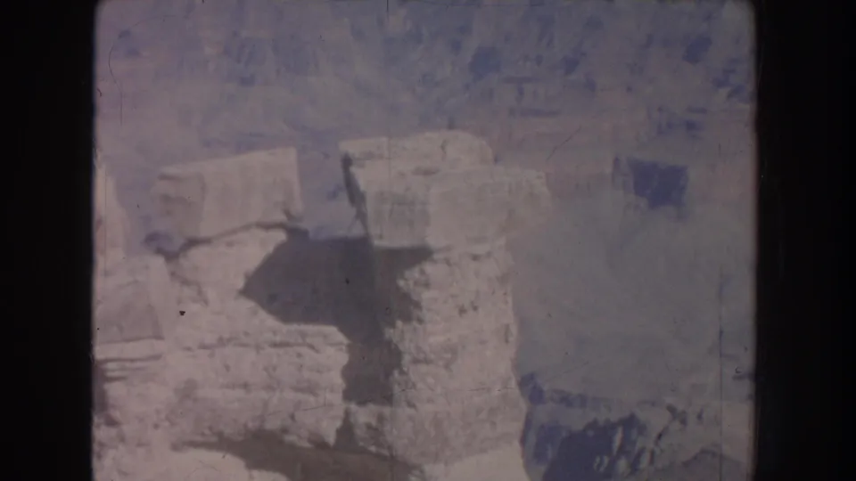 Faded 8mm frame of pale canyon rock and shadowed depth at a New Mexico overlook, with tourists no longer clearly visible.