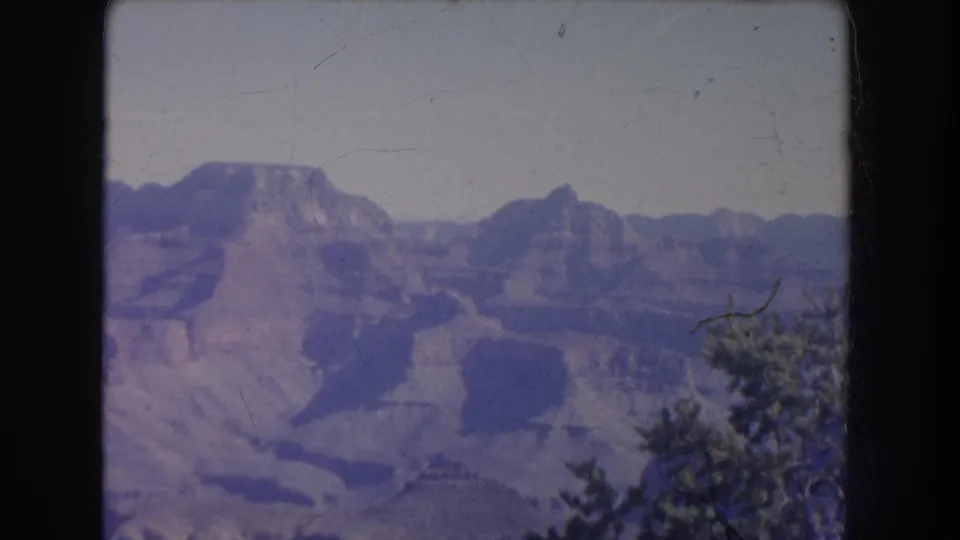 1951 New Mexico 8mm frame looking across distant canyon walls and mesas, with hazy sky and foreground vegetation.