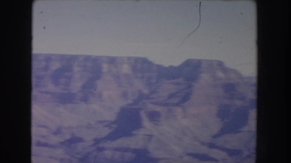 1951 New Mexico 8mm frame showing a wide view of canyon ridges and flat-topped formations beneath a pale sky.
