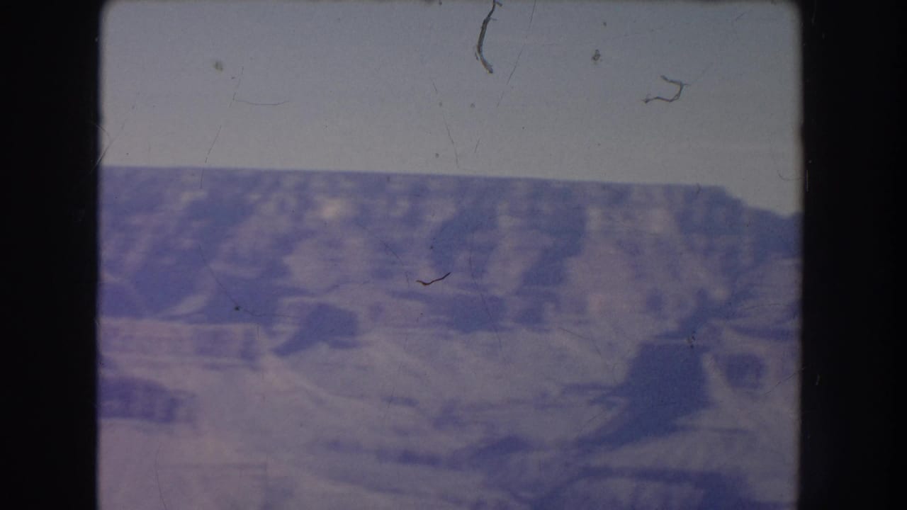 Soft view of a rocky canyon under a pale sky with dark 8mm film borders.