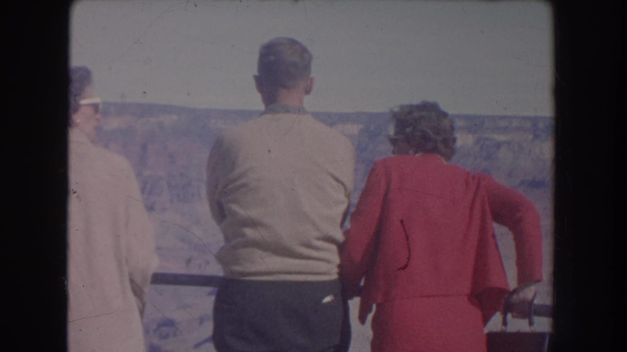 Three people stand at an overlook railing, facing a rocky canyon landscape.