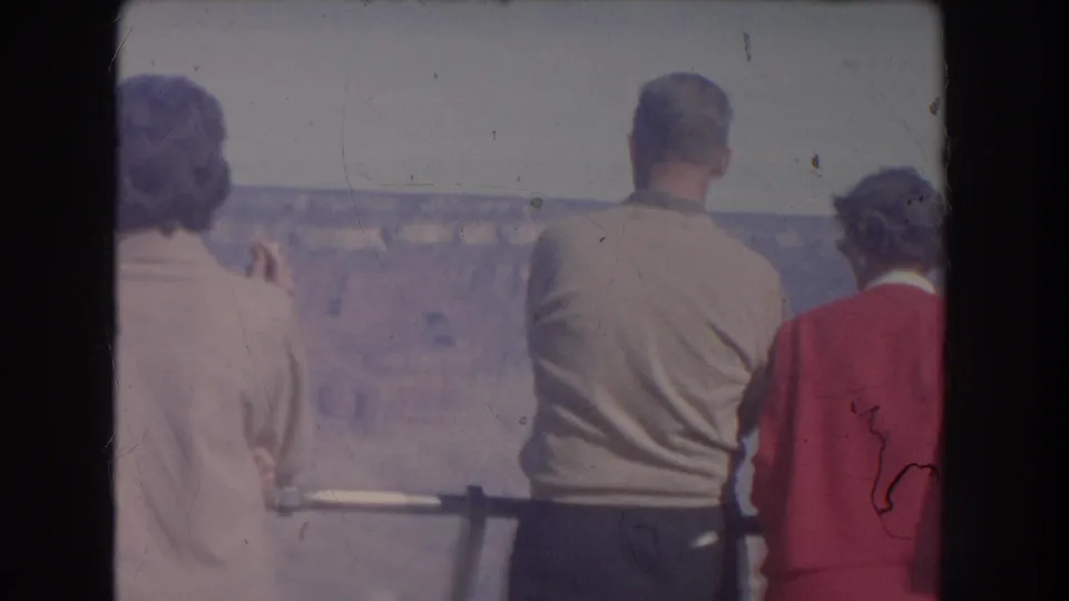 1951 New Mexico frame showing the family from behind at the overlook railing, with a rocky canyon and pale sky beyond.