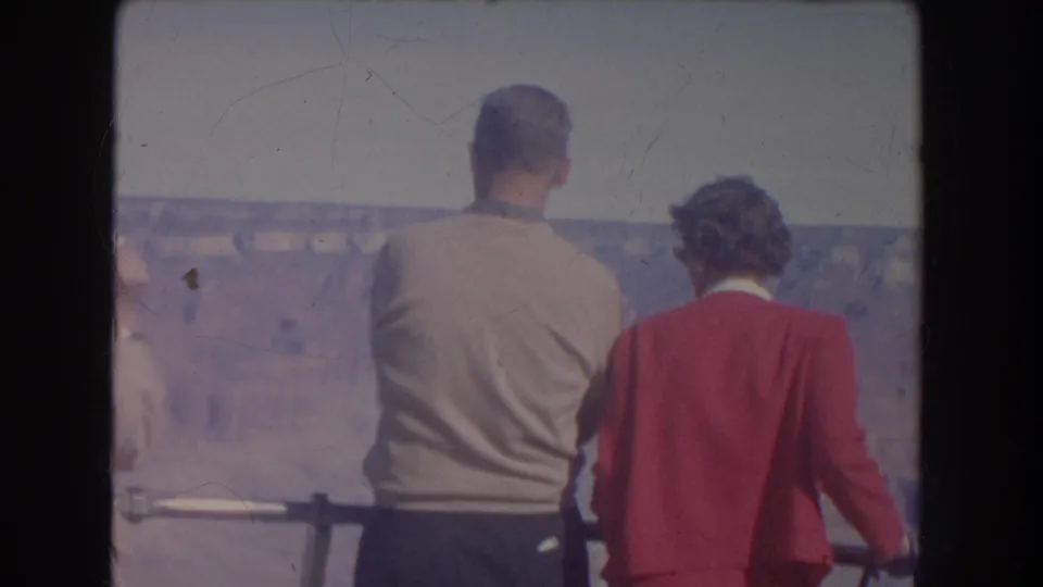 1951 New Mexico home-movie frame of tourists from behind, including a man in a light sweater and a woman in red, looking over a canyon.