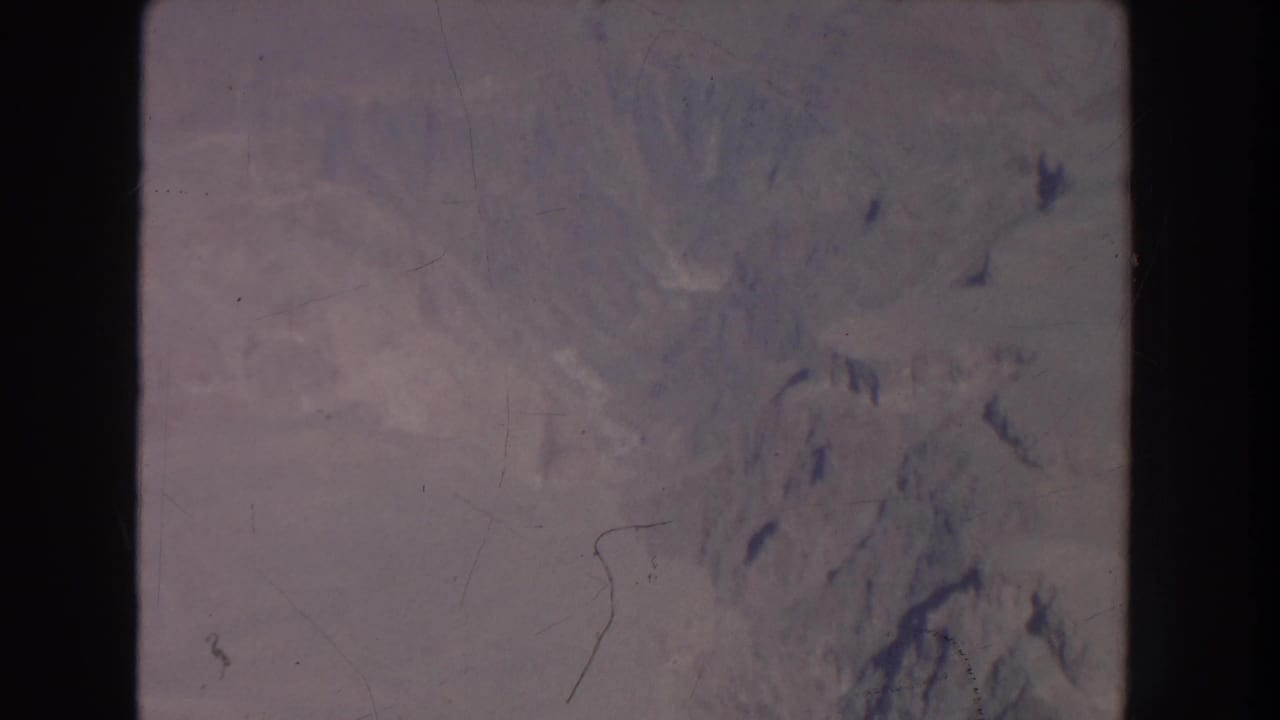 Soft aerial view of pale mountain terrain with film scratches and dark frame borders.