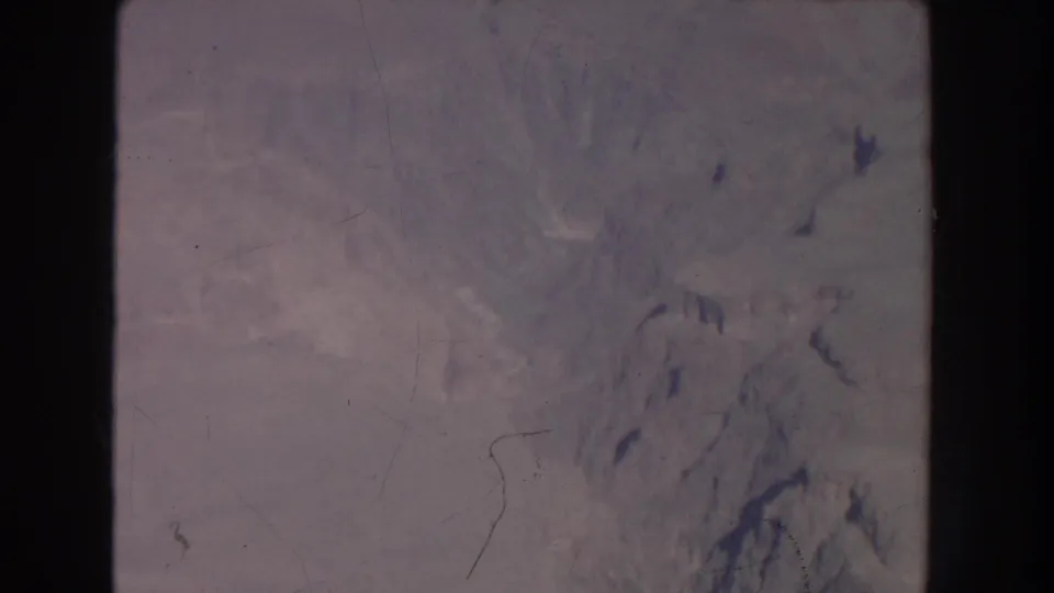 1951 New Mexico 8mm frame showing a soft aerial view of rugged pale mountain terrain with visible scratches and edge shadowing.