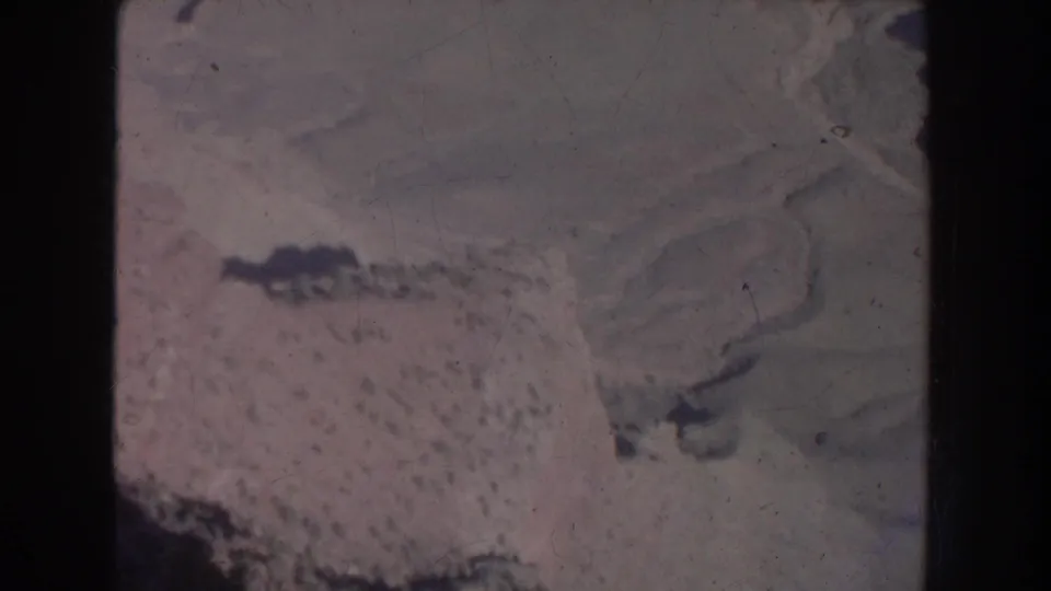 1951 New Mexico 8mm aerial frame showing textured mountain or desert terrain with darker landforms and pronounced film scratches.