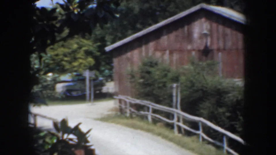 1952 California farm scene with a dirt road, white rail fence, red wooden barn, shrubs, trees, and a partial horse silhouette at the frame edge.