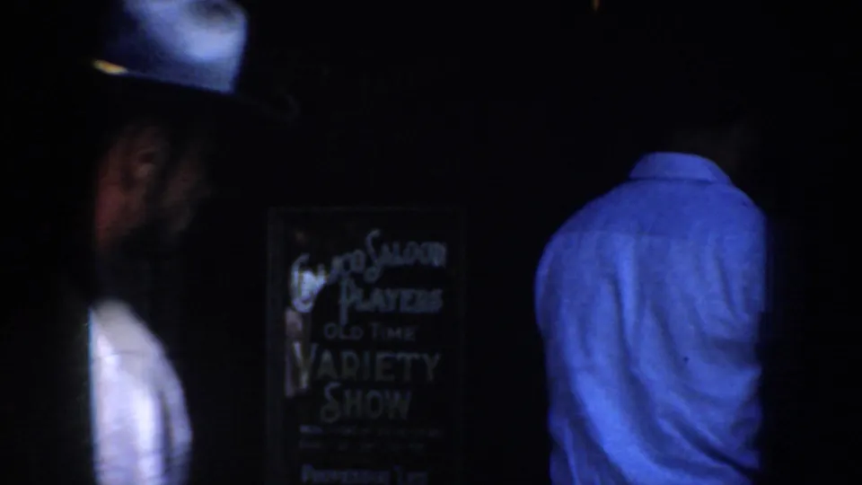 Dim 8mm frame from the same 1952 California clip, with two adults seen from behind or in profile near a hand-lettered old-time variety show sign.
