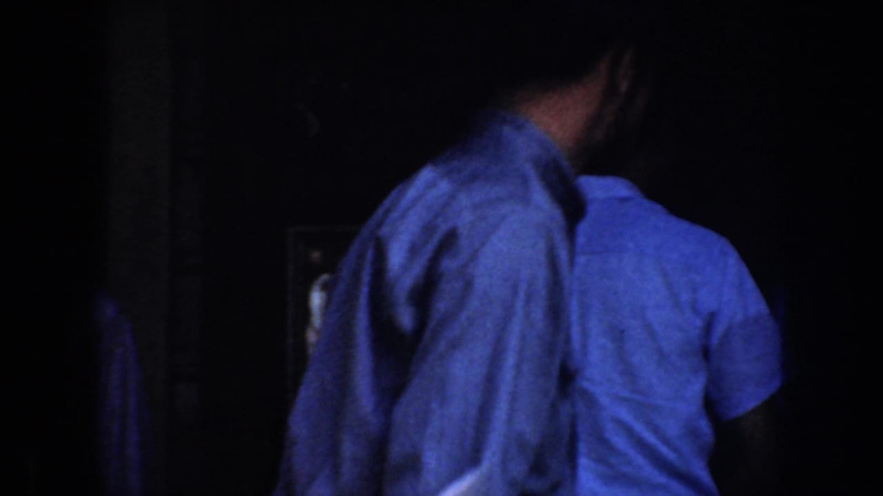 1952 California 8mm frame showing adults in shirts near a dark cabin-like entrance under blue night exposure.