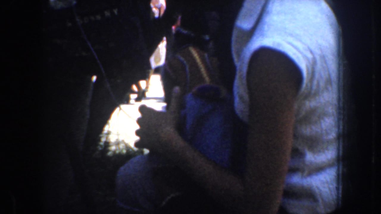 1952 California home-movie frame looking from a shaded interior past people toward a bright roadside area.