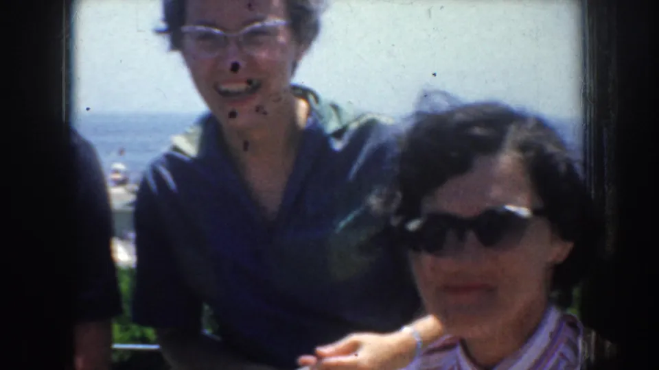 Two women laugh or smile near the California shore, with one wearing eyeglasses and another wearing dark sunglasses in the foreground.