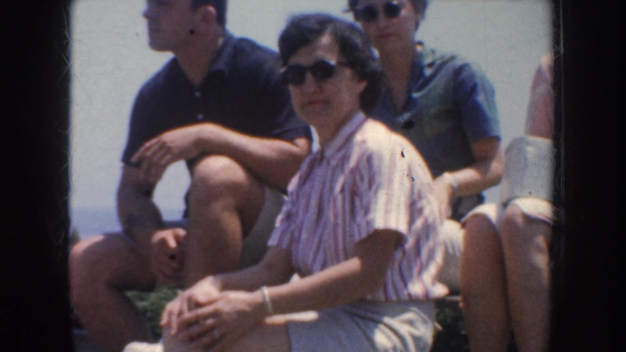 1952 California home-movie frame showing adults seated outdoors, including a woman in a striped blouse and sunglasses.