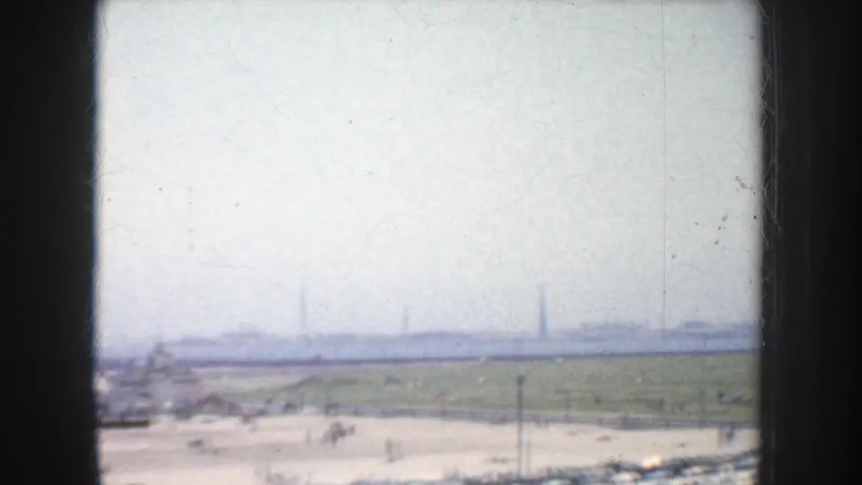 Hazy 1952 California home-movie frame looking toward a beach, with pale sand, distant figures, and heavy exposure flare.