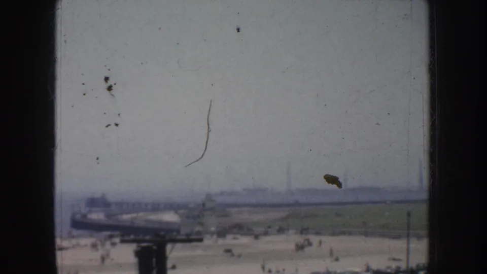 1952 California home-movie frame showing a hazy beach and pier area with distant people and visible 8mm film wear.