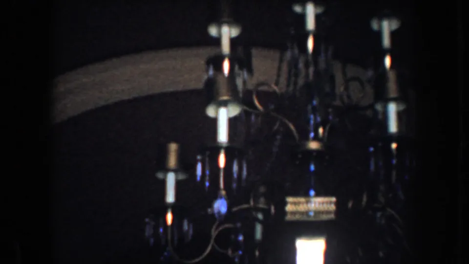 1952 California 8mm frame showing an ornate chandelier lit inside a dim private home interior.