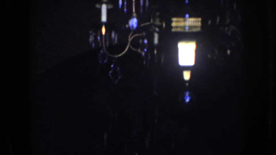 Dim 1952 California home-movie frame with a chandelier and bright bulbs receding into shadow.