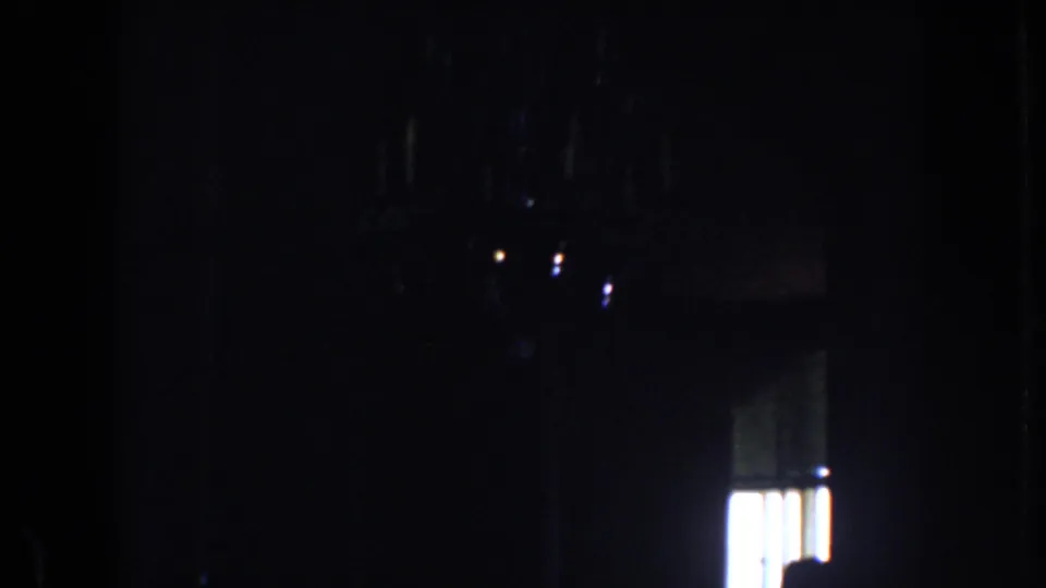 Low-exposure 8mm frame from a private California interior, with chandelier reflections above a bright window.